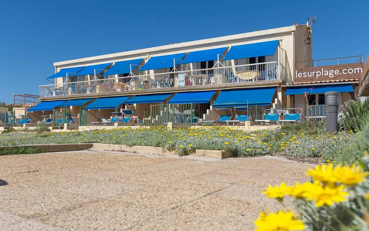 Façade du Surplage avec balcons et stores bleus face à la plage